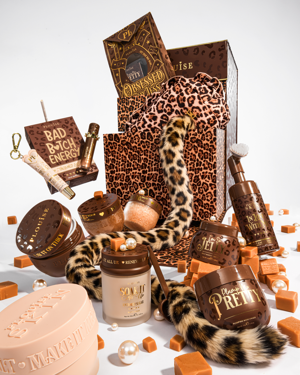 Un lussuoso set regalo di bellezza con elementi marroni e leopardati, tra cui un sacchetto regalo con stampa leopardata, una coda leopardata e diversi contenitori per cosmetici nei toni del marrone e del beige, disposti su uno sfondo bianco con cubetti e perle color caramello.