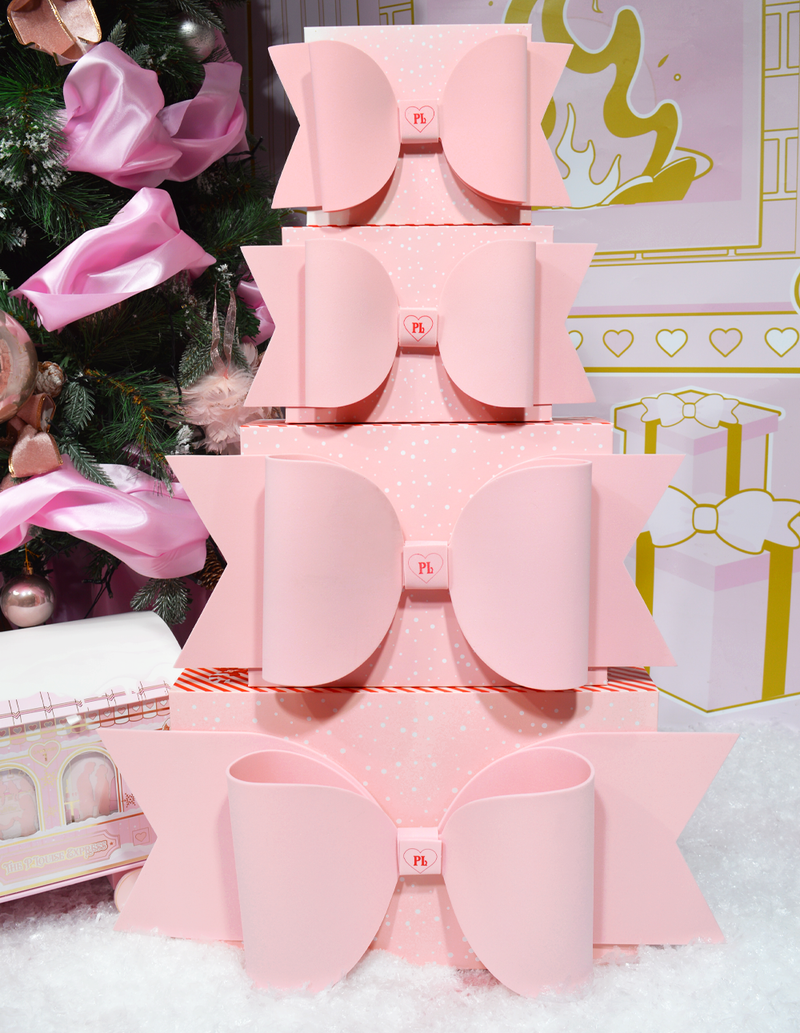 Pila di scatole regalo rosa P.Louise con fiocchi esposti su uno sfondo a tema natalizio con decorazioni.