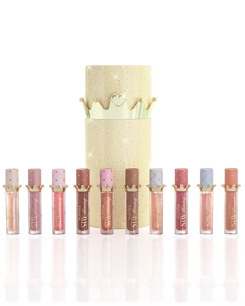 Un set di dieci prodotti P.Louise Christmas Stay Shining Lip Oil disposti in fila davanti a una scatola cilindrica color oro scintillante con un coperchio dorato a corona, su uno sfondo bianco pulito.