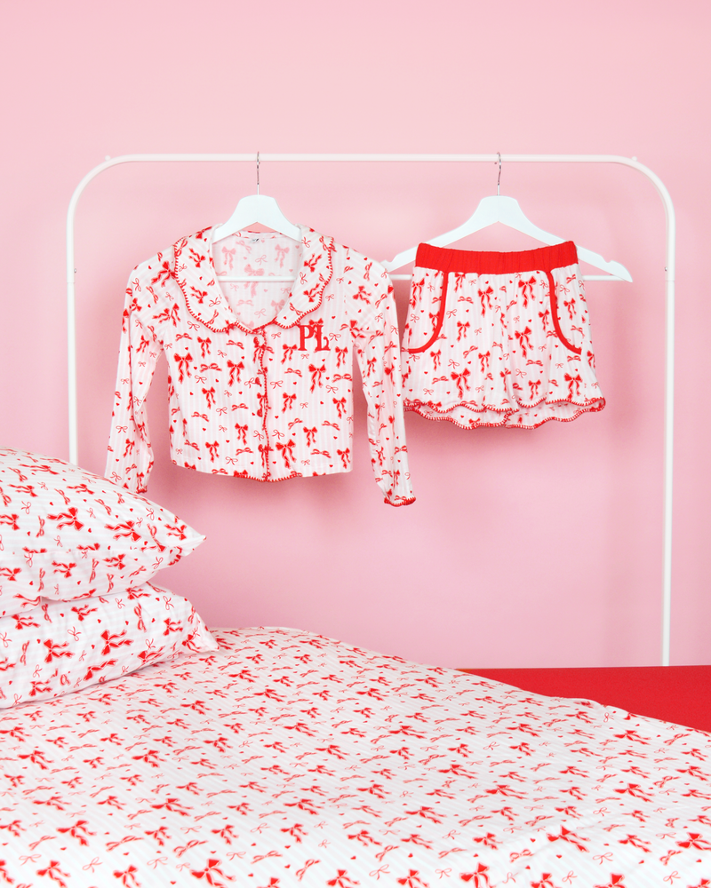 Set of pink and white striped girls P.Louise Christmas bow pyjamas shorts on hangers in a pink bedroom with matching bedding