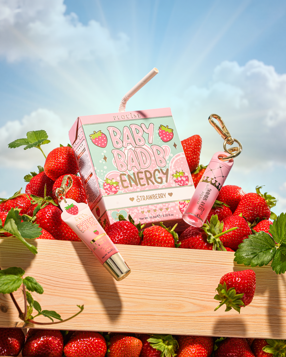 P.Louise Strawberry Baby Bad B Mini Lip Oil e Mini Lip Conditioner su un tavolo circondato da fragole