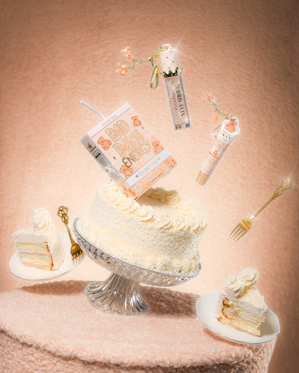 Una torta su un tavolo di stoffa di peluche con un P.Louise Teddy Glitter Bad Bitch Energy Lip Duo in una torta al cocco contenente un balsamo per labbra e un olio per labbra che galleggiano intorno alla torta
