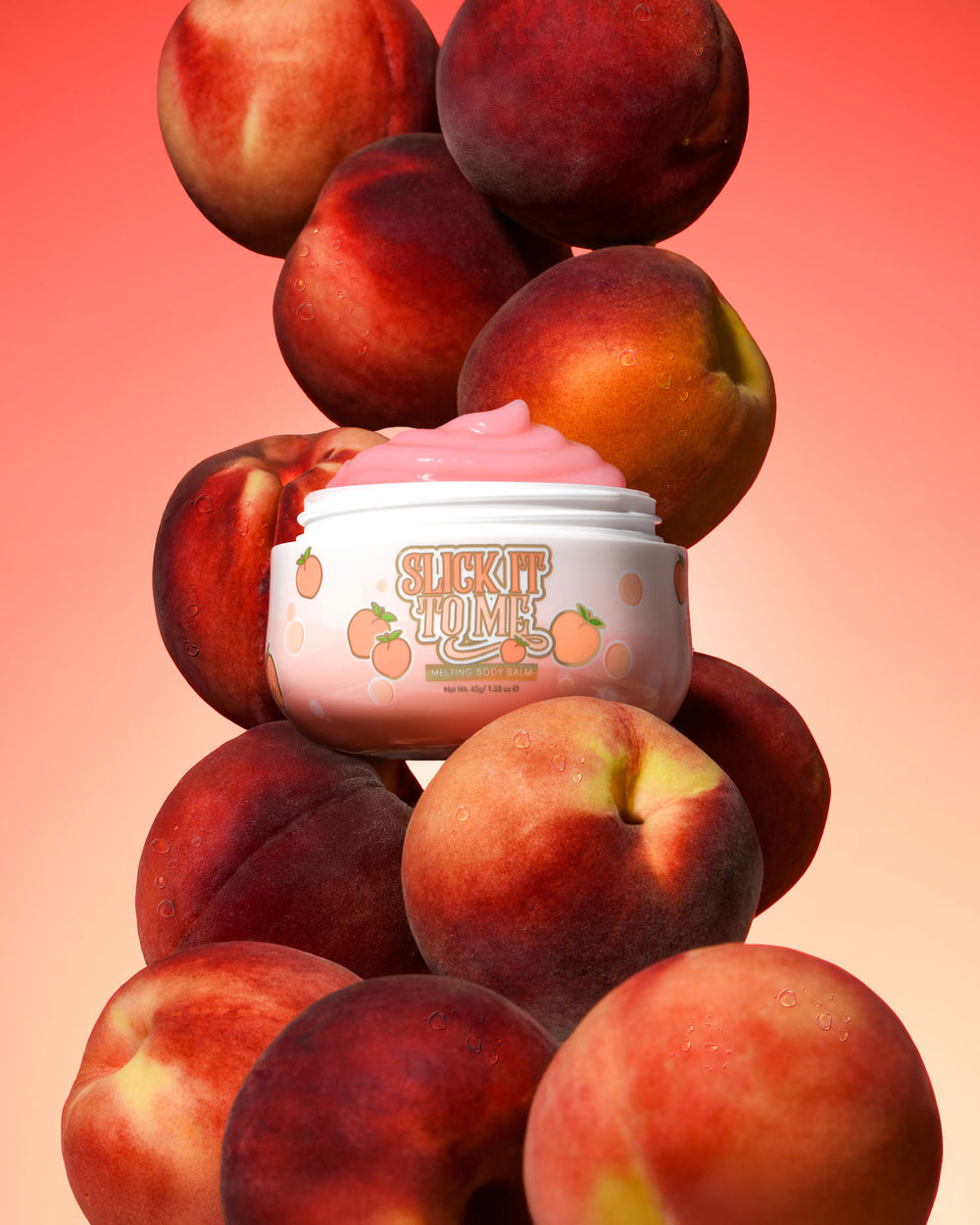Vasetto di balsamo corpo fondente alla pesca Slick It To Me P. Louise con crema rosa circondata da pesche su sfondo sfumato