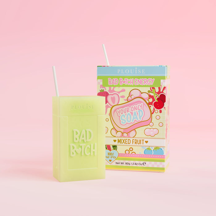 Una saponetta verde con inciso "Bad Bitch", accompagnata da una confezione di succhi colorati con l'etichetta "Mixed Fruit", presentata su uno sfondo rosa.