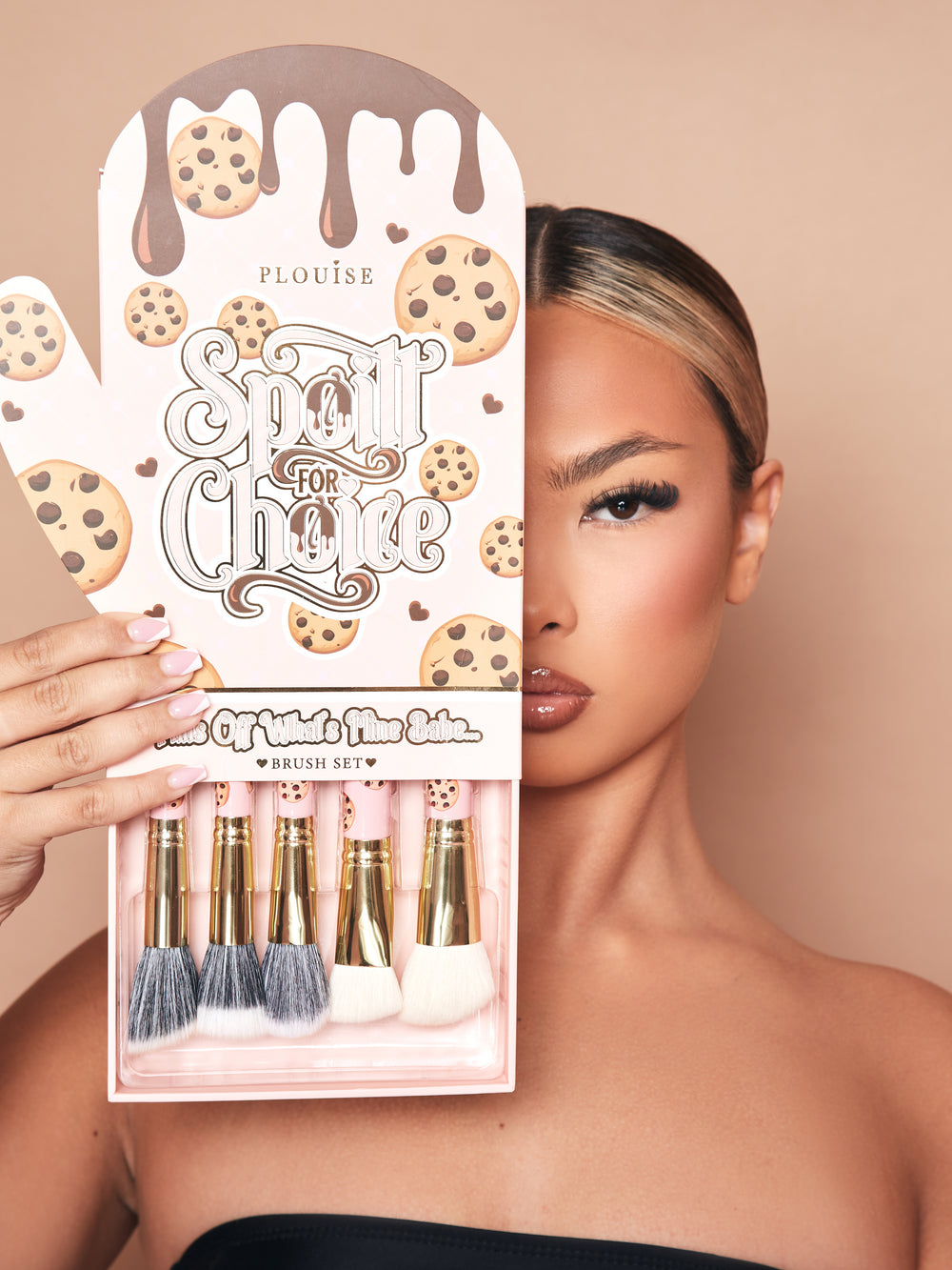 Un'immagine del set di pennelli per trucco da 5 pezzi Spoiled For Choice di P.Louise in una scatola di guanti da forno con un vassoio estratto dal fondo che mostra parzialmente i pennelli. La confezione mostra metà del volto della modella truccata