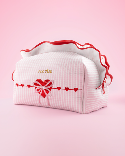 Una borsa per il trucco e la cura della pelle P.Louise a strisce rosa e bianche con fronzoli e un disegno a forma di cuore su uno sfondo rosa