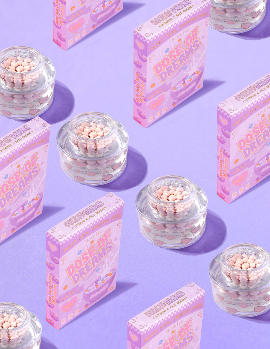Contenitori trasparenti di P.Louise DOse of Dreams Viatmin C Capsule Face Cream con capsule rosa al loro interno circondate da scatole di cereali rosa su sfondo viola