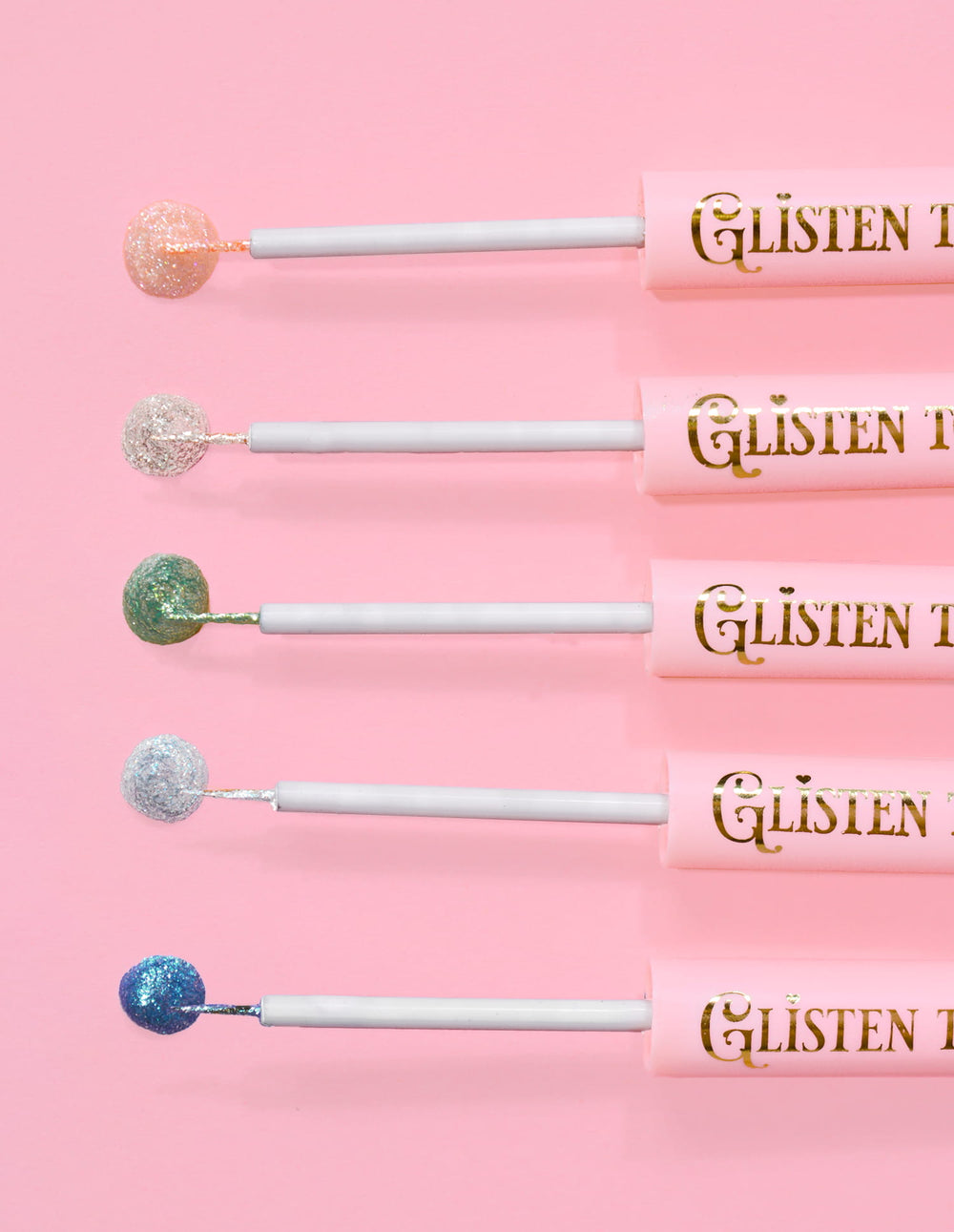 5 eyeliner glitter P.Louise Glisten To Your Heart allineati con una goccia di prodotto sull'estremità su uno sfondo rosa