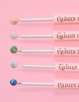 5 eyeliner glitter P.Louise Glisten To Your Heart allineati con una goccia di prodotto sull'estremità su uno sfondo rosa