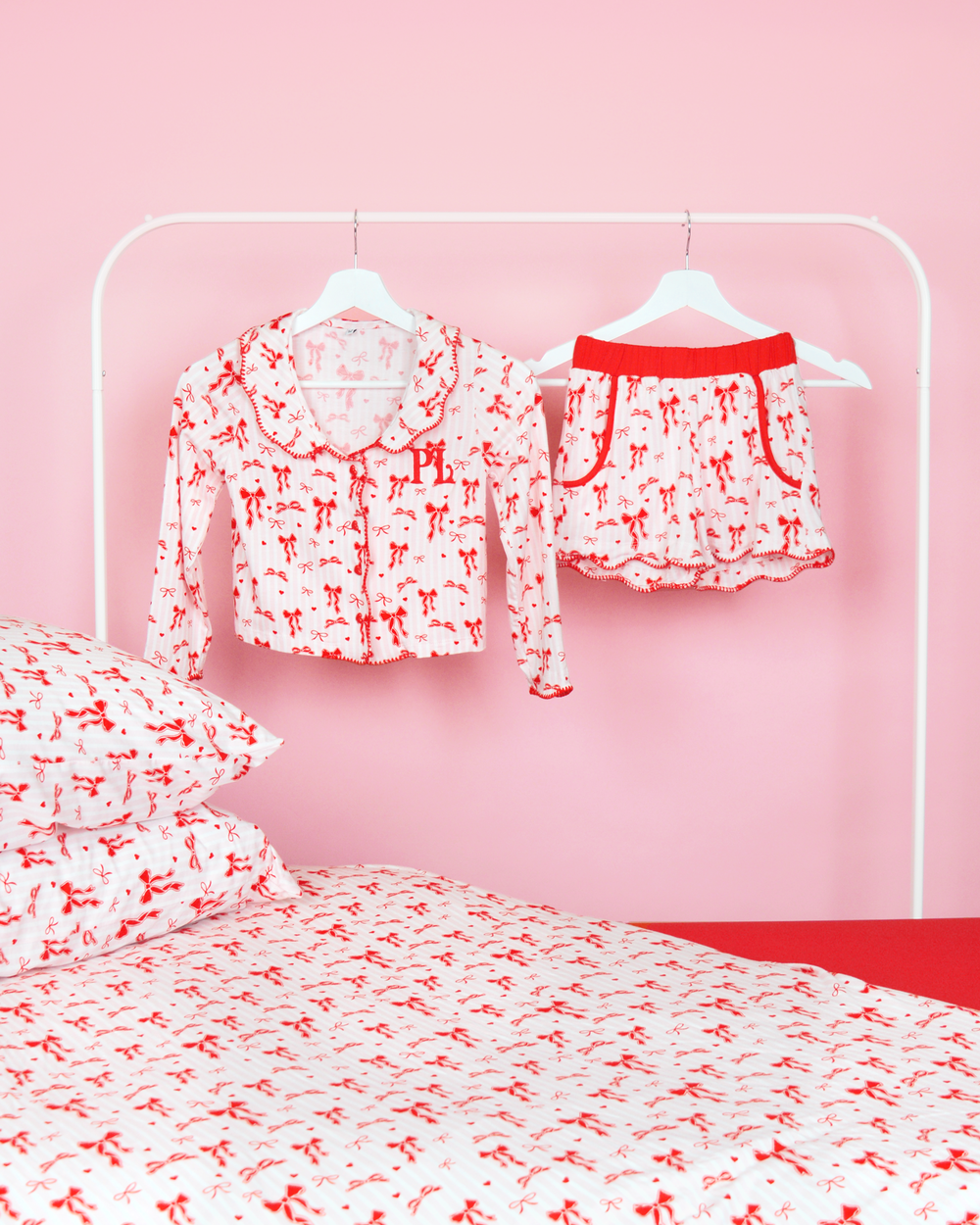 Set di pantaloncini del pigiama natalizio P.Louise a righe bianche e rosa per ragazze appesi sulle grucce in una camera da letto rosa con biancheria da letto abbinata 