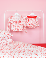 Set di pantaloncini del pigiama natalizio P.Louise a righe bianche e rosa per ragazze appesi sulle grucce in una camera da letto rosa con biancheria da letto abbinata 