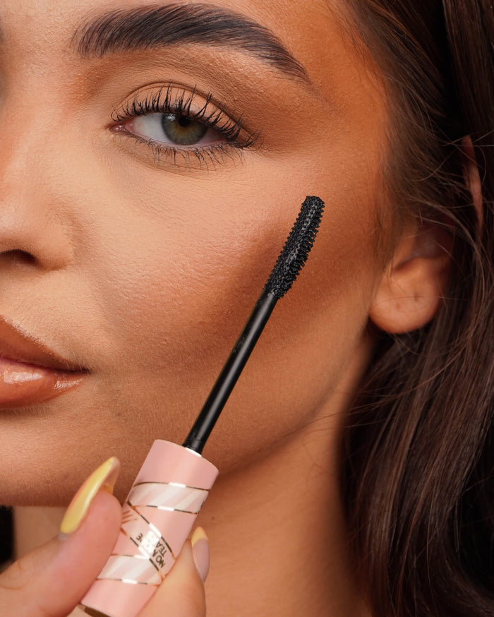 Primo piano di un bastoncino di mascara P.Louise Tearproof tenuto vicino all'occhio di una persona con uno sfondo sfocato