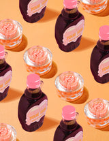 Contenitori trasparenti di crema in capsule alla vitamina C P.Louise Dose of Dreams con capsule arancioni al loro interno circondate da flaconi di sciroppo viola e rosa su sfondo arancione