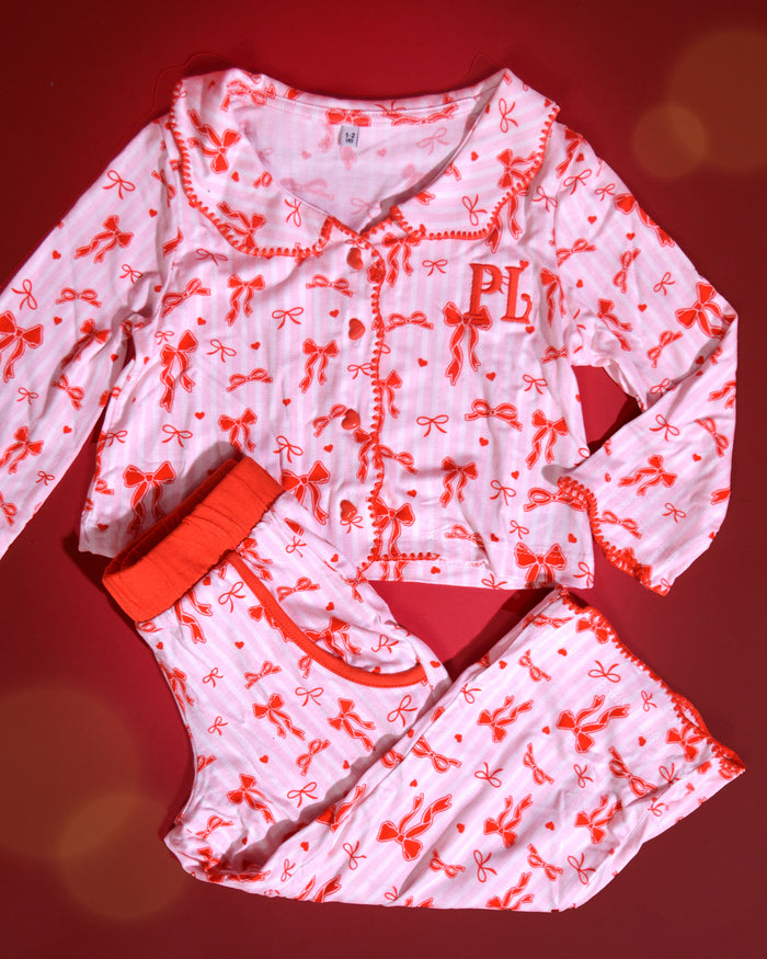 Set di pigiami natalizi per bambini a righe rosa e bianche con disegni di fiocchi rossi su uno sfondo rosso