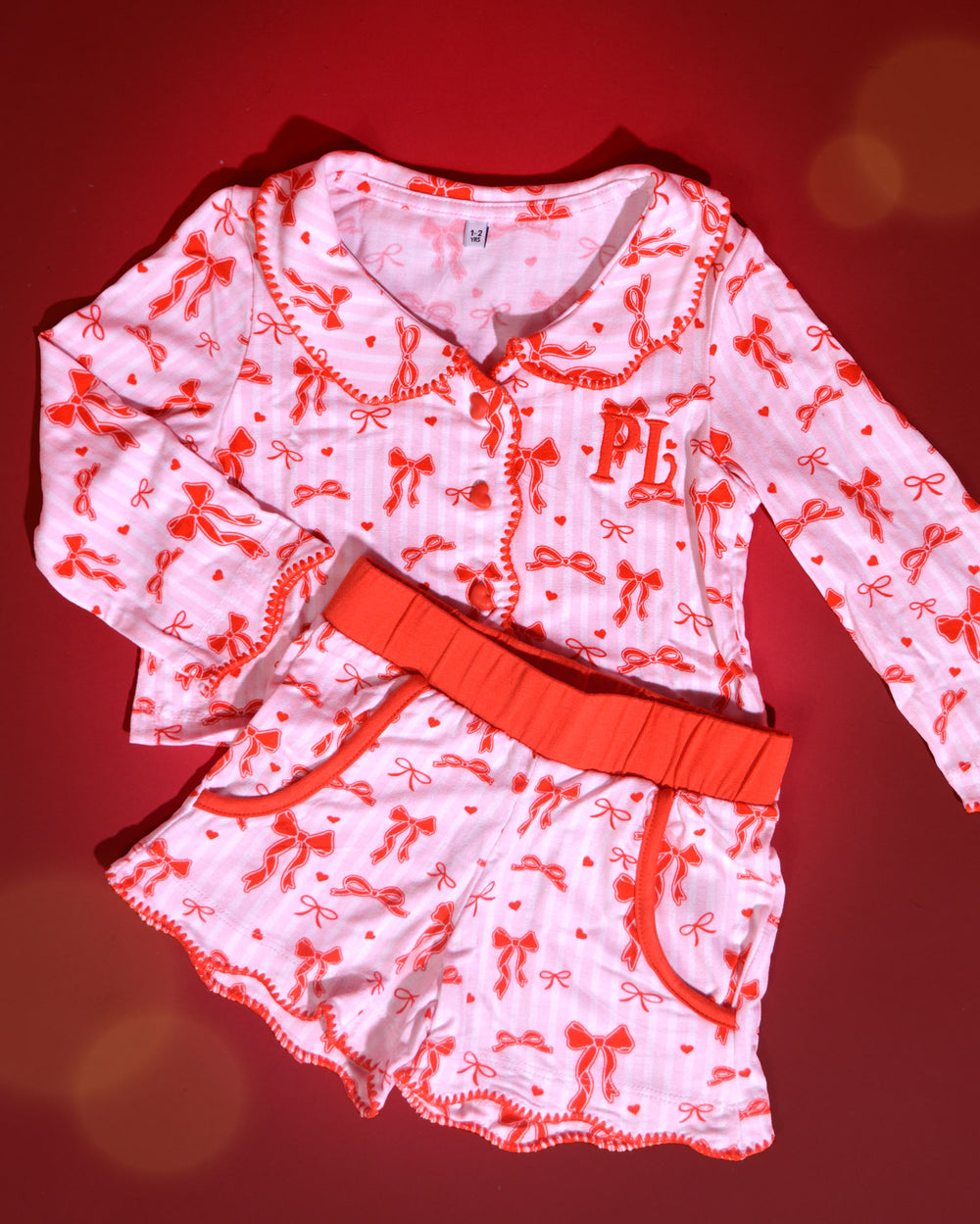Set di pigiami natalizi per bambini a righe rosa e bianche con disegni di fiocchi rossi su uno sfondo rosso