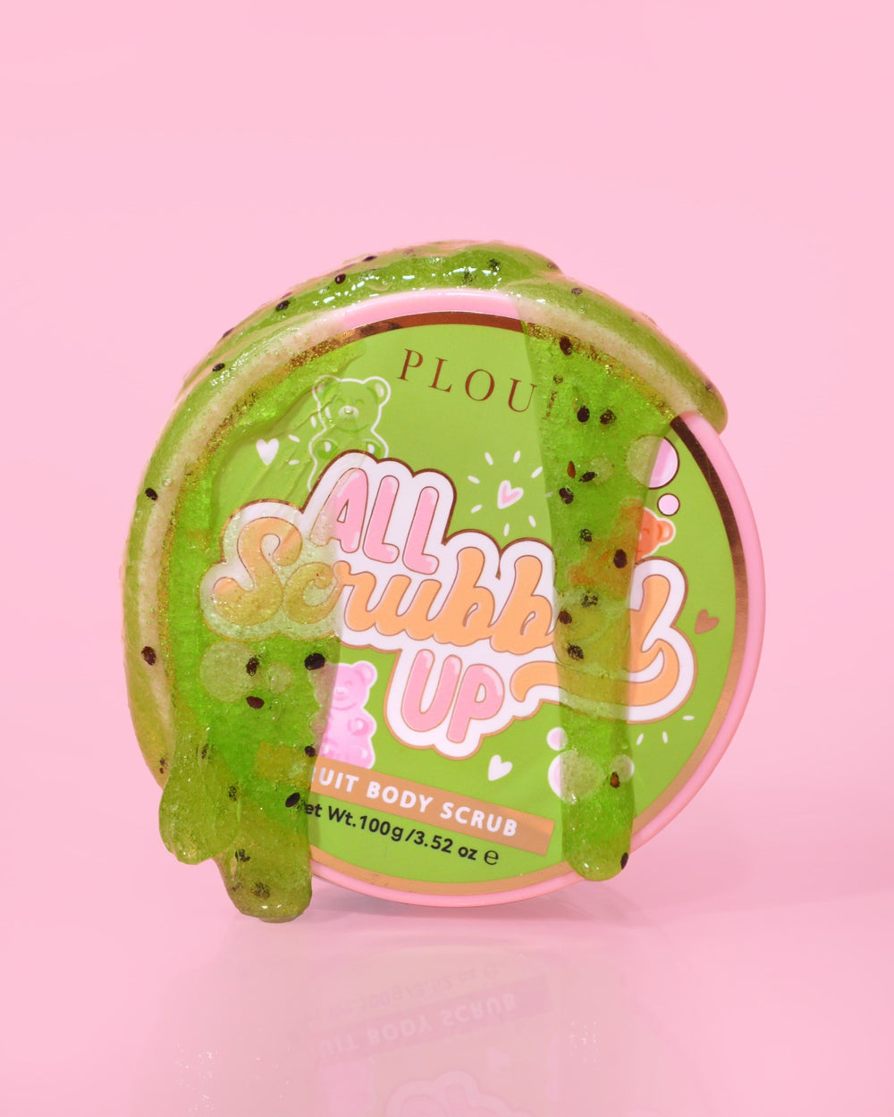Un contenitore di P.Louise All Scrubbed Up Body Scrub con l'etichetta "Candy Bears" su uno sfondo rosa, con il prodotto che appare come un gel verde