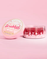 Vaso aperto di scrub corpo P. Louise All Scrubbed Up al frutto del drago su sfondo rosa