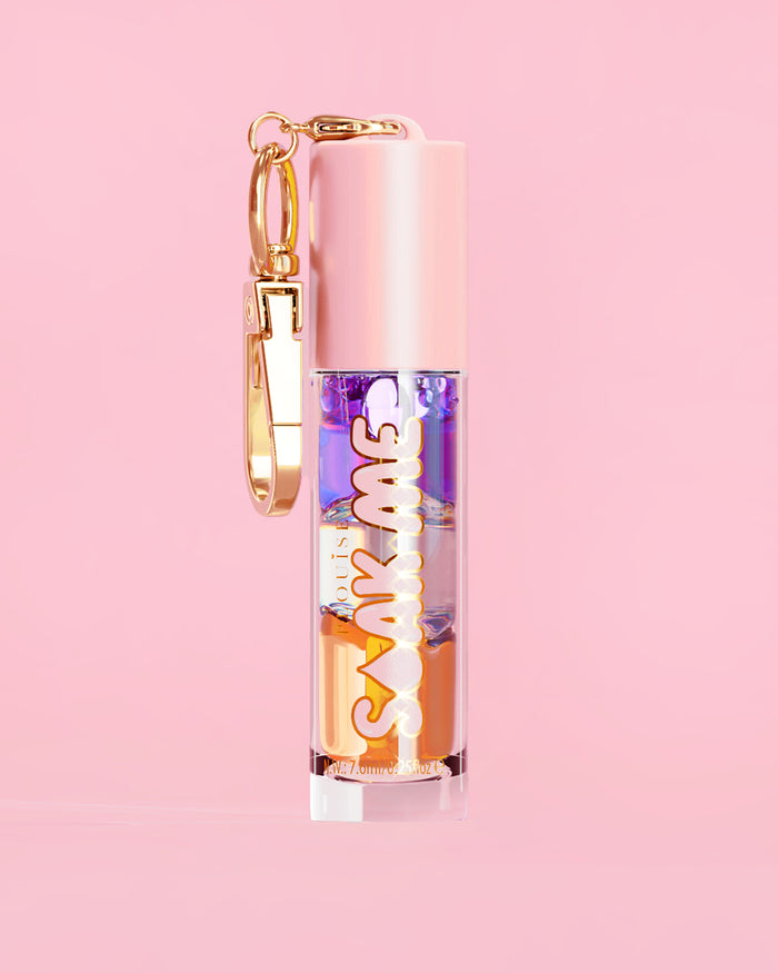 P. Louise Soak Me Lip Oil con strati di olio colorato in un tubo rosa con chiusura dorata su sfondo rosa