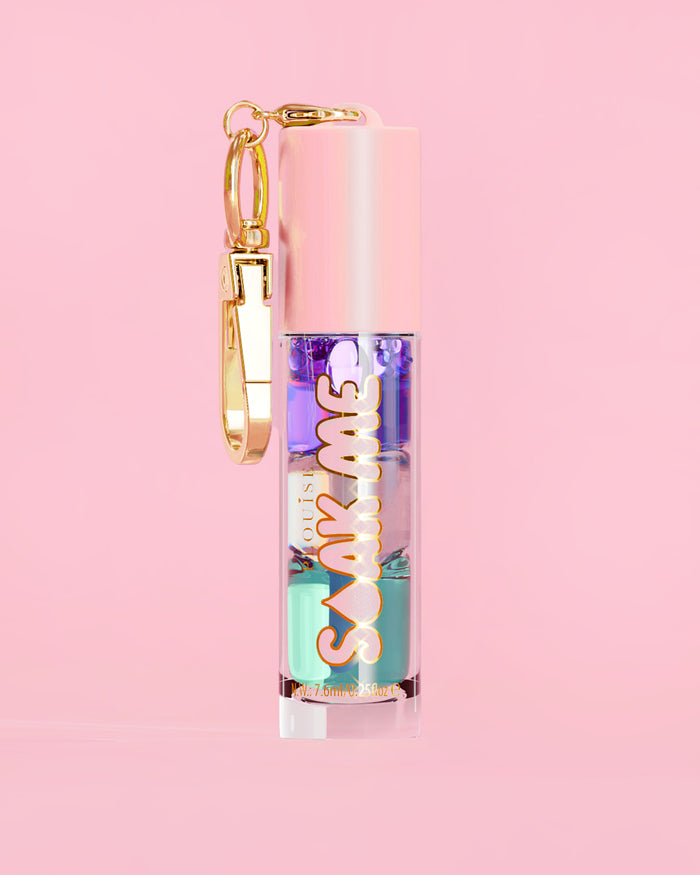 P. Louise Soak Me Lip Oil con strati di olio colorato in un tubo rosa con chiusura dorata su sfondo rosa