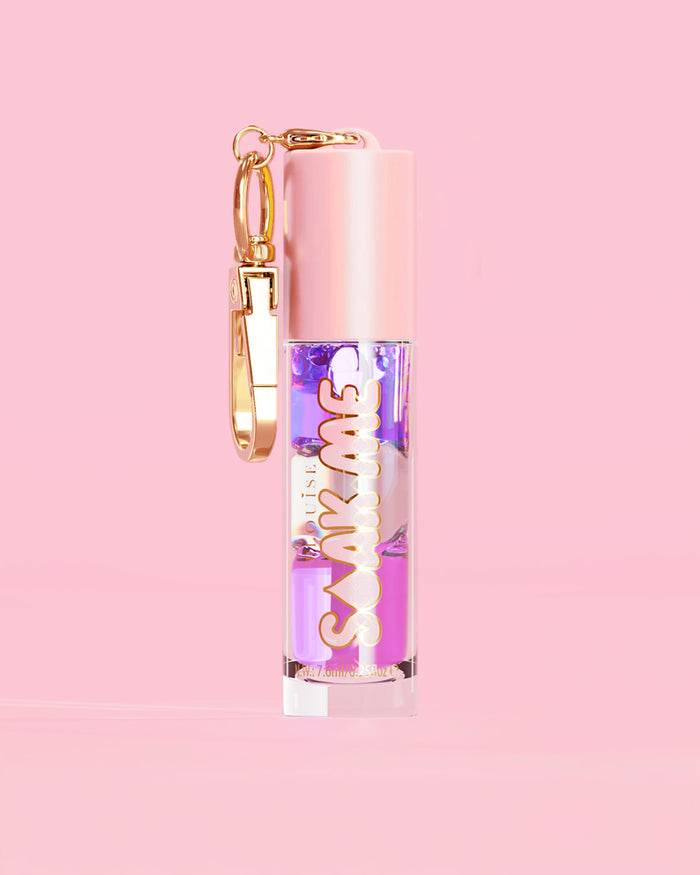 P. Louise Soak Me Lip Oil con strati di olio colorato in un tubo rosa con chiusura dorata su sfondo rosa