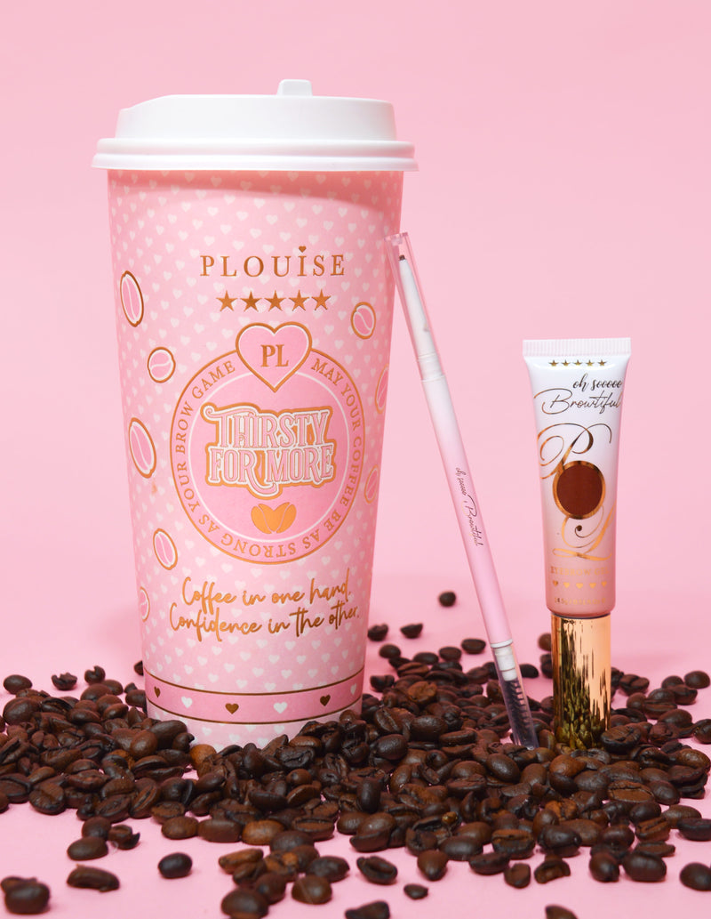 Un'immagine di prodotto che mostra una matita per sopracciglia a doppia punta accanto a un tubetto di gel per sopracciglia, esposta su una superficie rosa con chicchi di caffè sparsi qua e là. Lo sfondo ha una tazza di caffè rosa con elementi di branding.