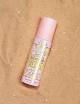 Un flacone di spray fissante opacizzante P.Louise Fix Up con tappo rosa e motivi decorativi sull'etichetta, esposti su una superficie sabbiosa.