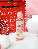 Una bottiglia di spray fissante P. Louise Ready Set Sparkle Christmas Glitter circondato da decorazioni festive come neve, palline e una cassetta delle lettere natalizie