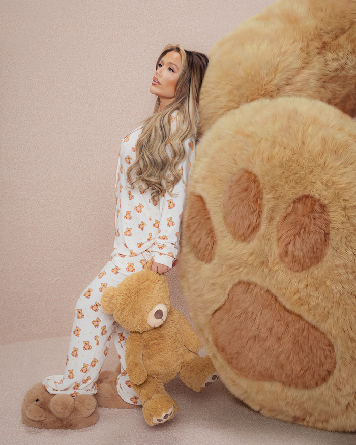 Donna in pigiama di orsacchiotto che tiene un orsacchiotto accanto a una grande zampa di orso di peluche su uno sfondo beige