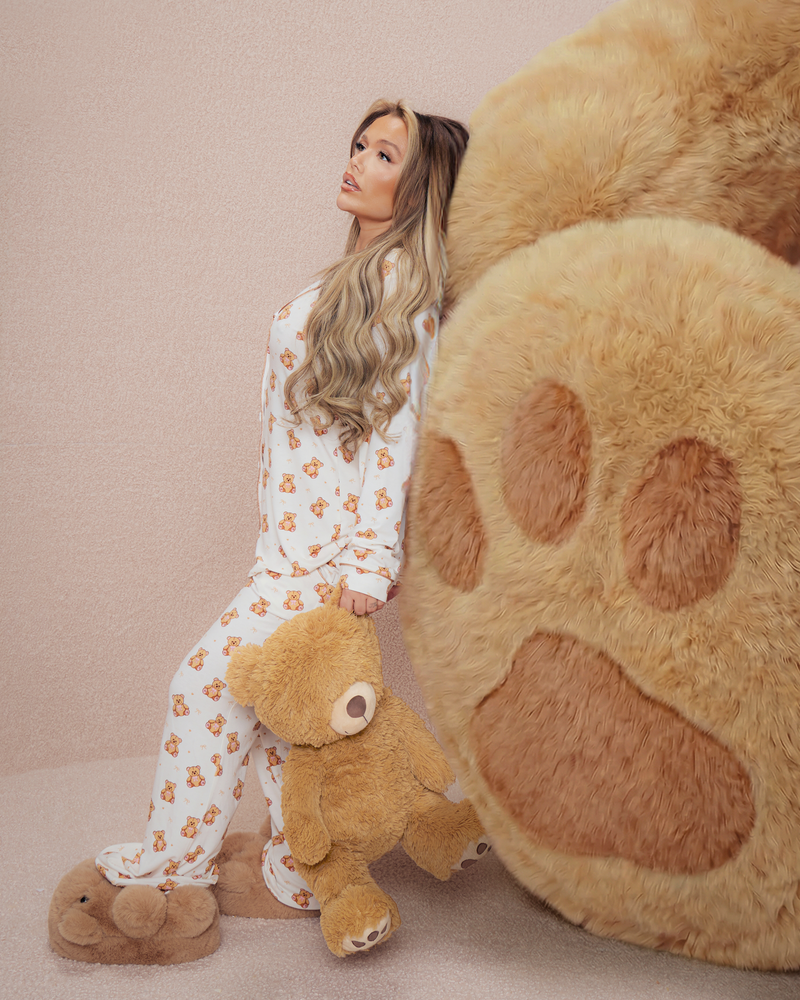 Donna in pigiama di orsacchiotto che tiene un orsacchiotto accanto a una grande zampa di orso di peluche su uno sfondo beige
