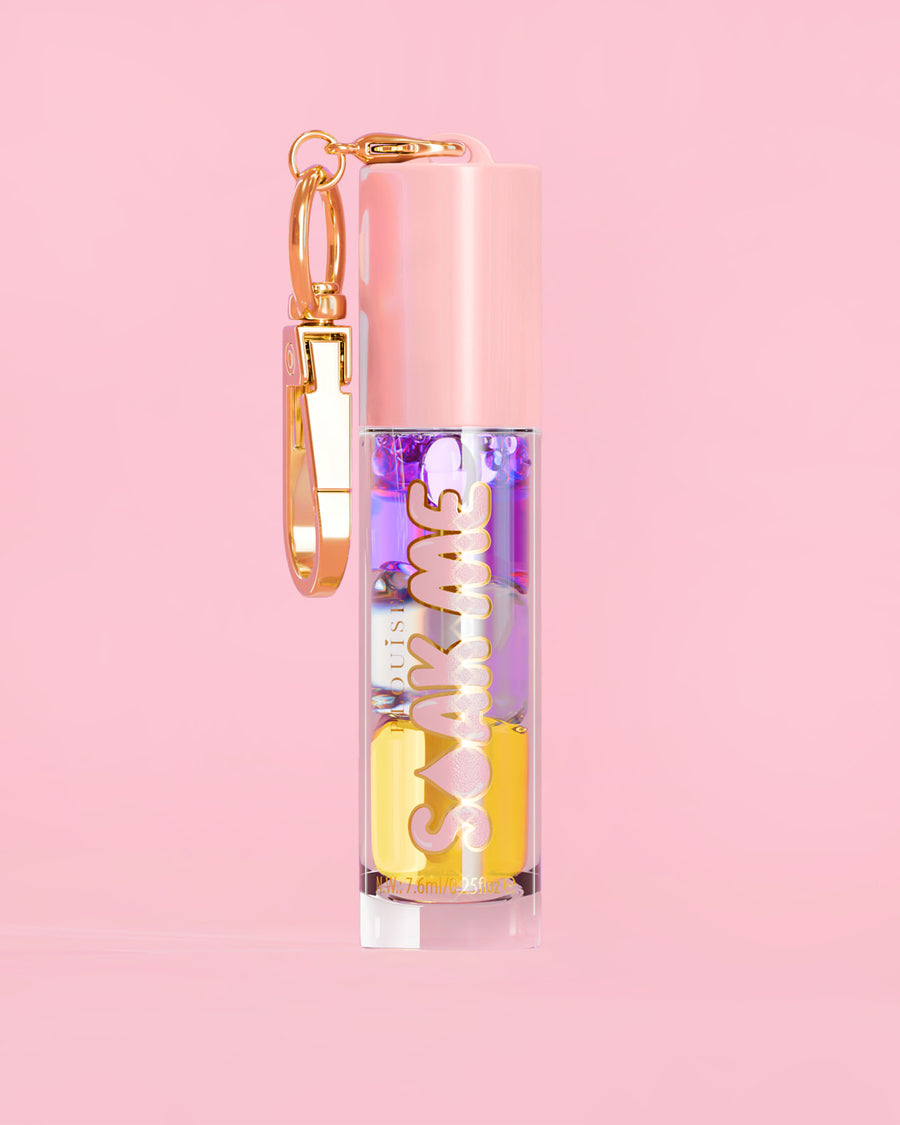 P. Louise Soak Me Lip Oil con strati di olio colorato in un tubo rosa con chiusura dorata su sfondo rosa