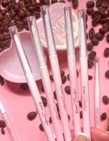 Una collezione di matite per sopracciglia P.Louise rosa con pennelli a spoolie, esposte insieme a chicchi di caffè e un piatto rosa.