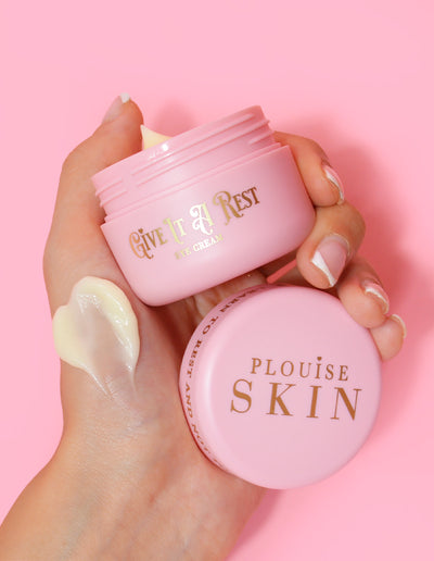 Una persona che tiene in mano un barattolo rosa di crema per gli occhi Give It A Rest di P.Louise senza il coperchio, mostrando il nome del prodotto e il marchio sul barattolo.
